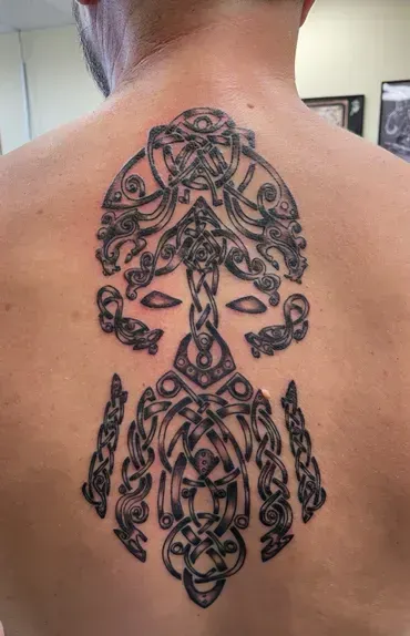 A man has a celtic tattoo on his back.