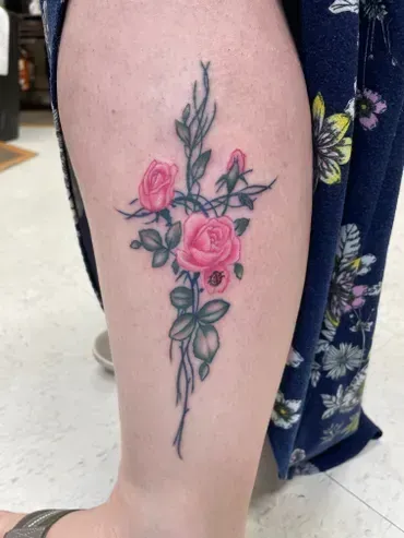A woman has a tattoo of a cross with pink roses on her leg.