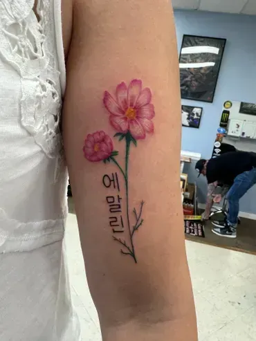 A woman has a tattoo of a pink flower on her arm.