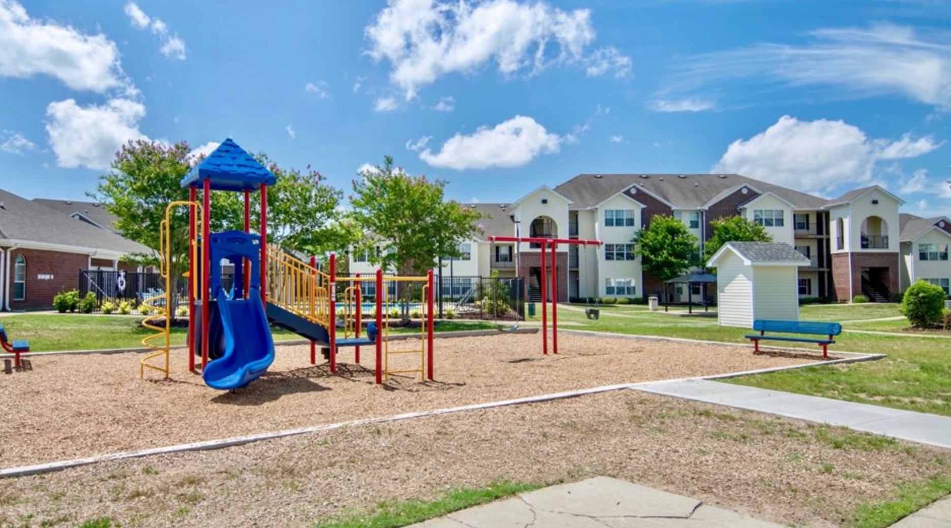 There is a playground in the middle of a park in front of a building.