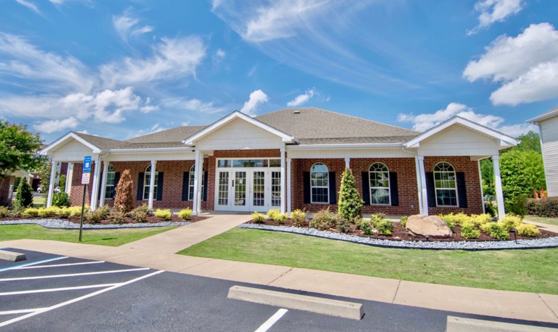 A large brick house with a white porch and a parking lot in front of it.