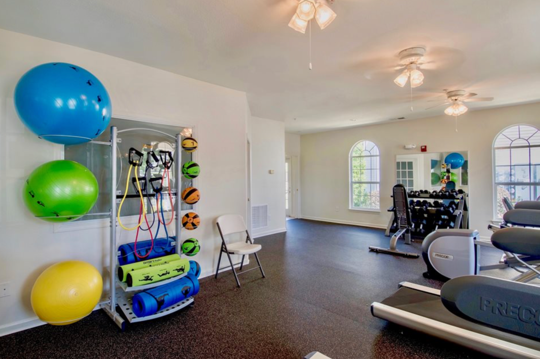 A gym with a treadmill , exercise balls , and a chair.
