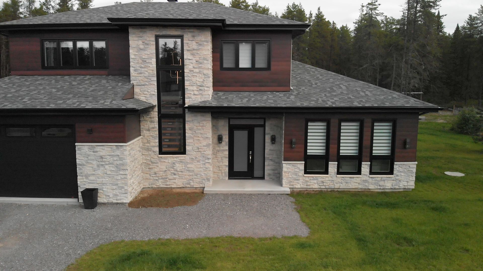 Une grande maison avec beaucoup de fenêtres et un toit gris se trouve au sommet d'un champ vert luxuriant.