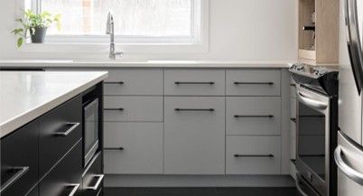 Une cuisine avec des armoires blanches, des tiroirs noirs, des appareils en acier inoxydable et une fenêtre.