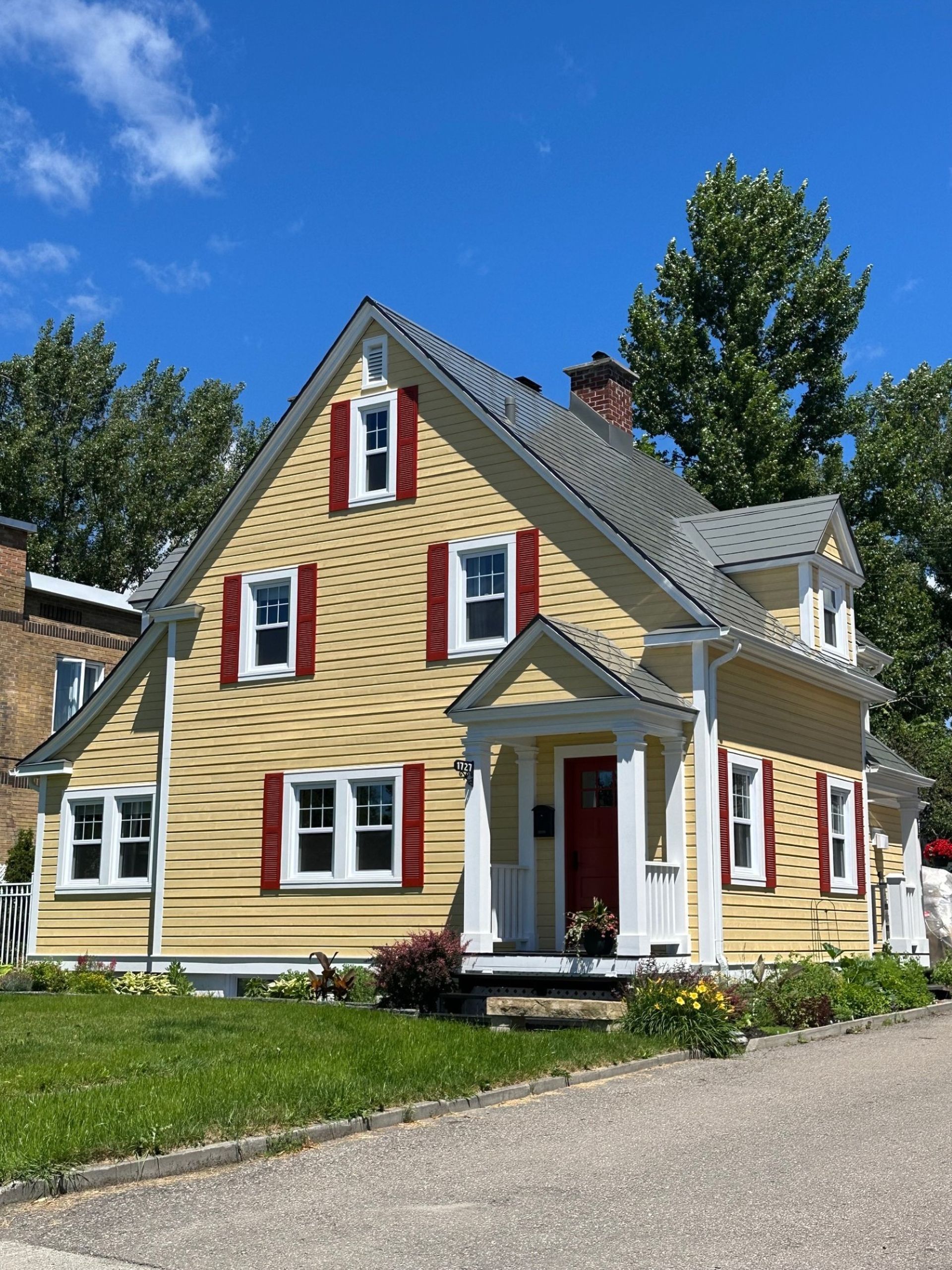 Une maison jaune avec des volets rouges aux fenêtres