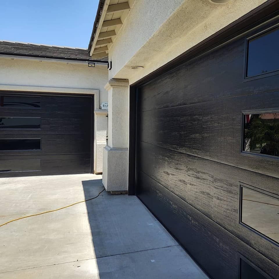 A light-colored garage door with small, dark windows, set against a stone-clad wall, part of a house.