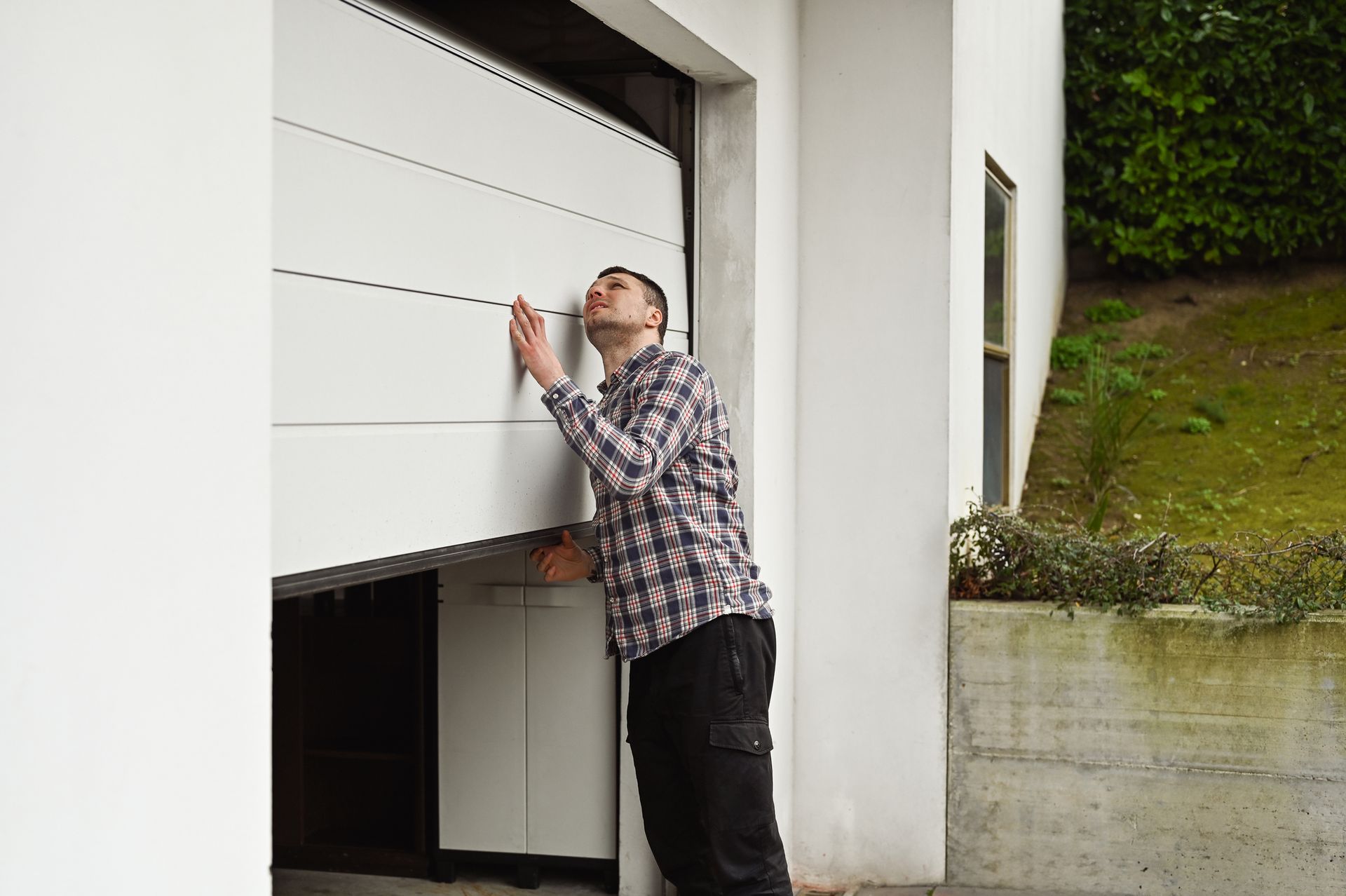 A man trying to lift his stuck garage door from the outside.