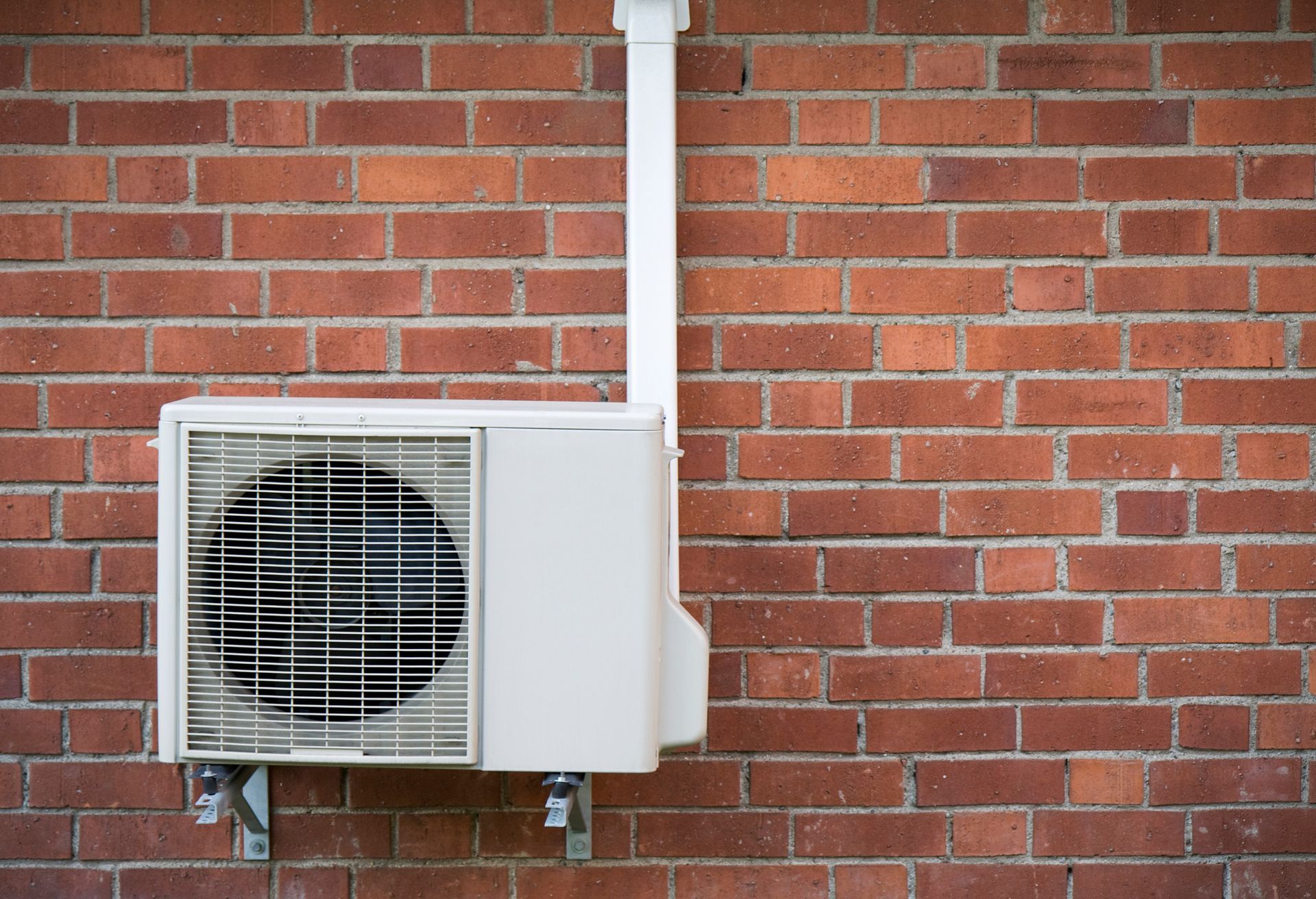 A white air conditioner is mounted to a red brick wall. A white air conditioner is mounted to a red brick wall.