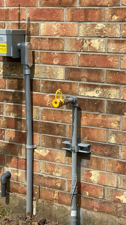A brick wall with a gray pipe and a yellow hose attached to it.