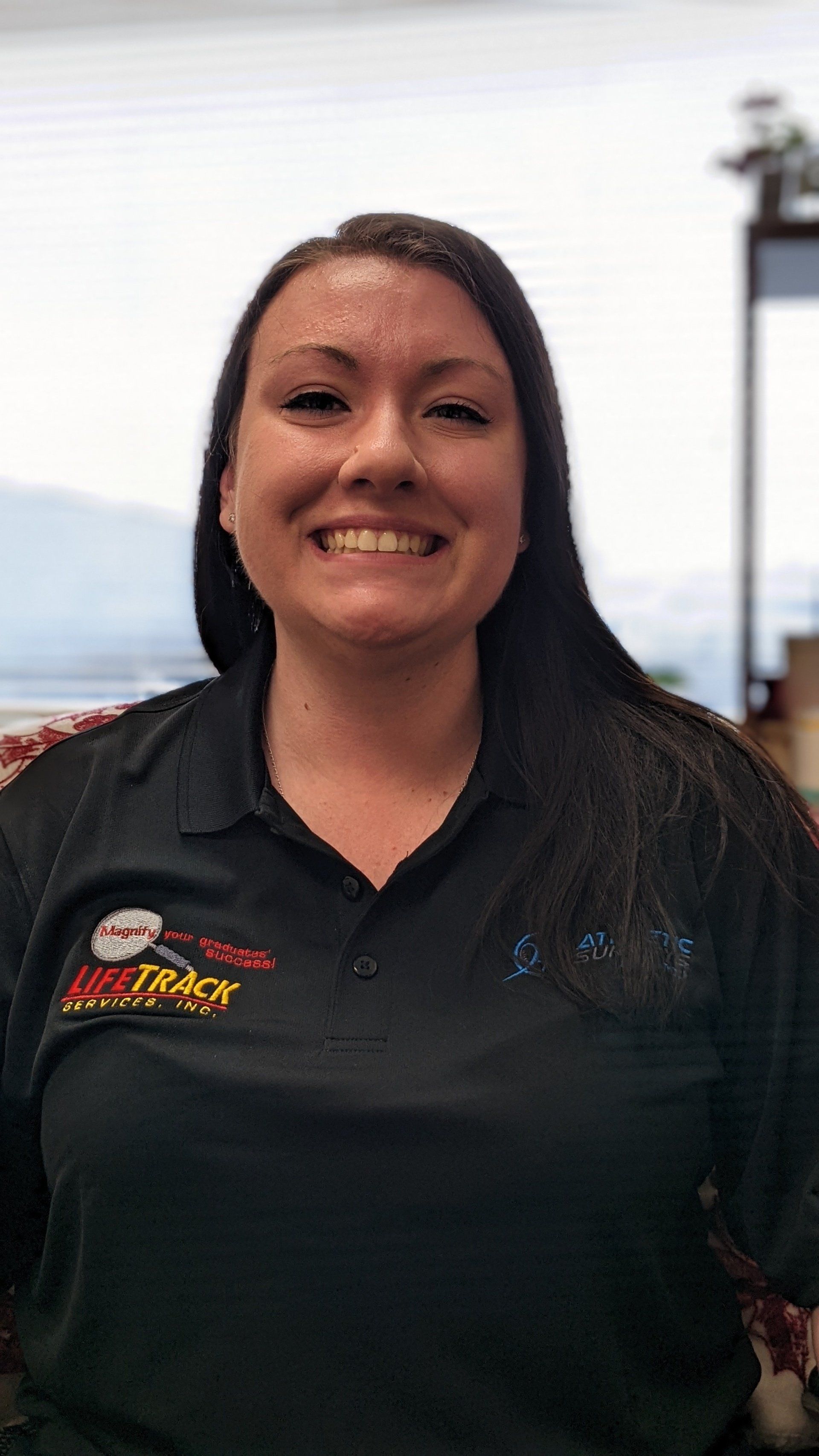 Woman with long dark hair, wearing a black shirt with logo, smiling.