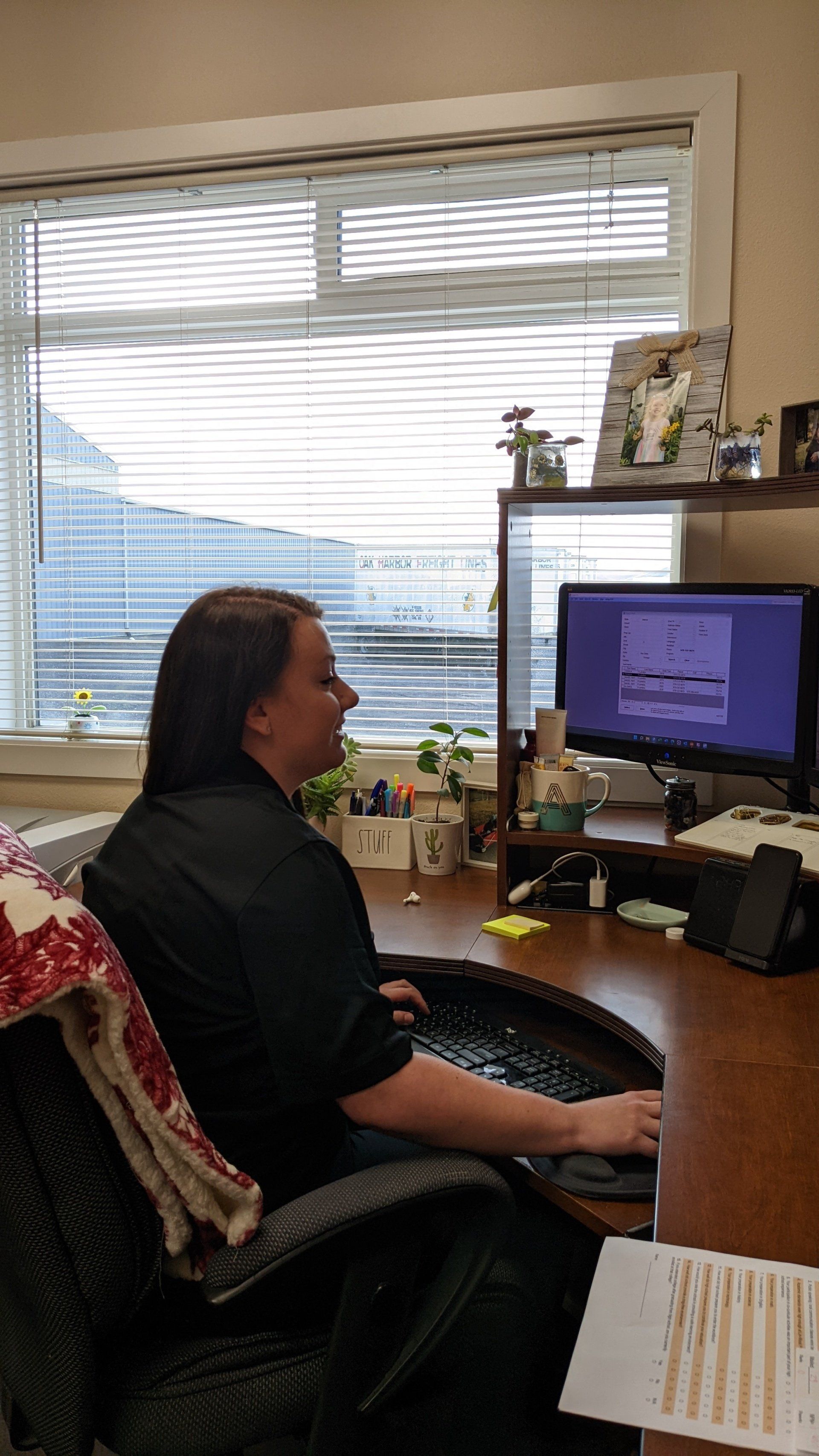Woman seated at a desk, facing a computer screen in an office setting.
