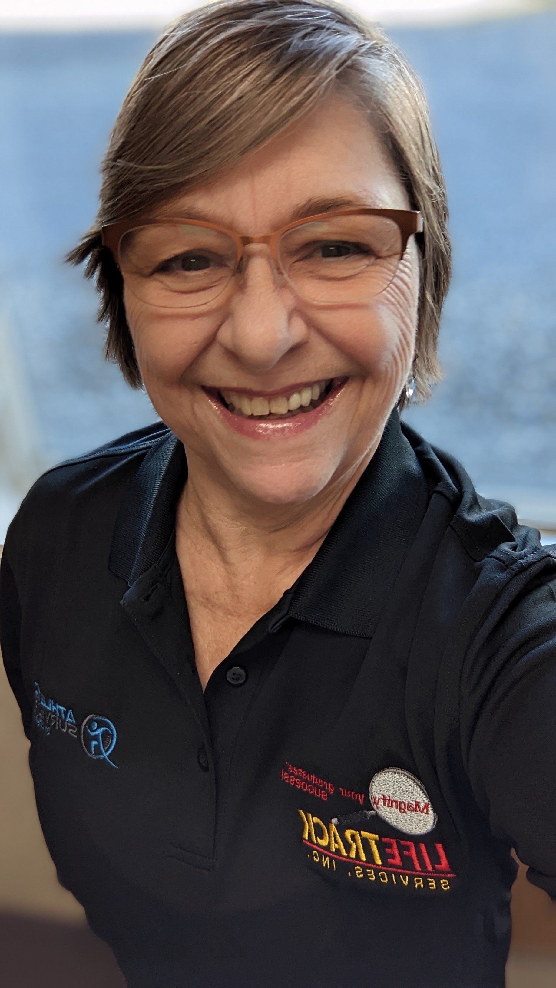 Woman with glasses smiles broadly, wearing a black shirt with logos.