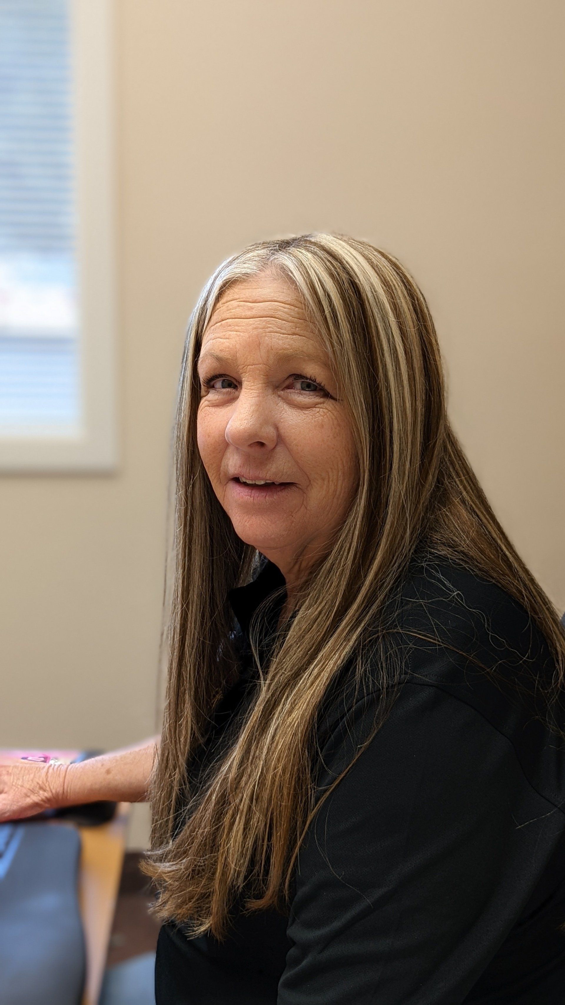 Woman with long brown hair, slight smile, seated indoors, looking towards camera.