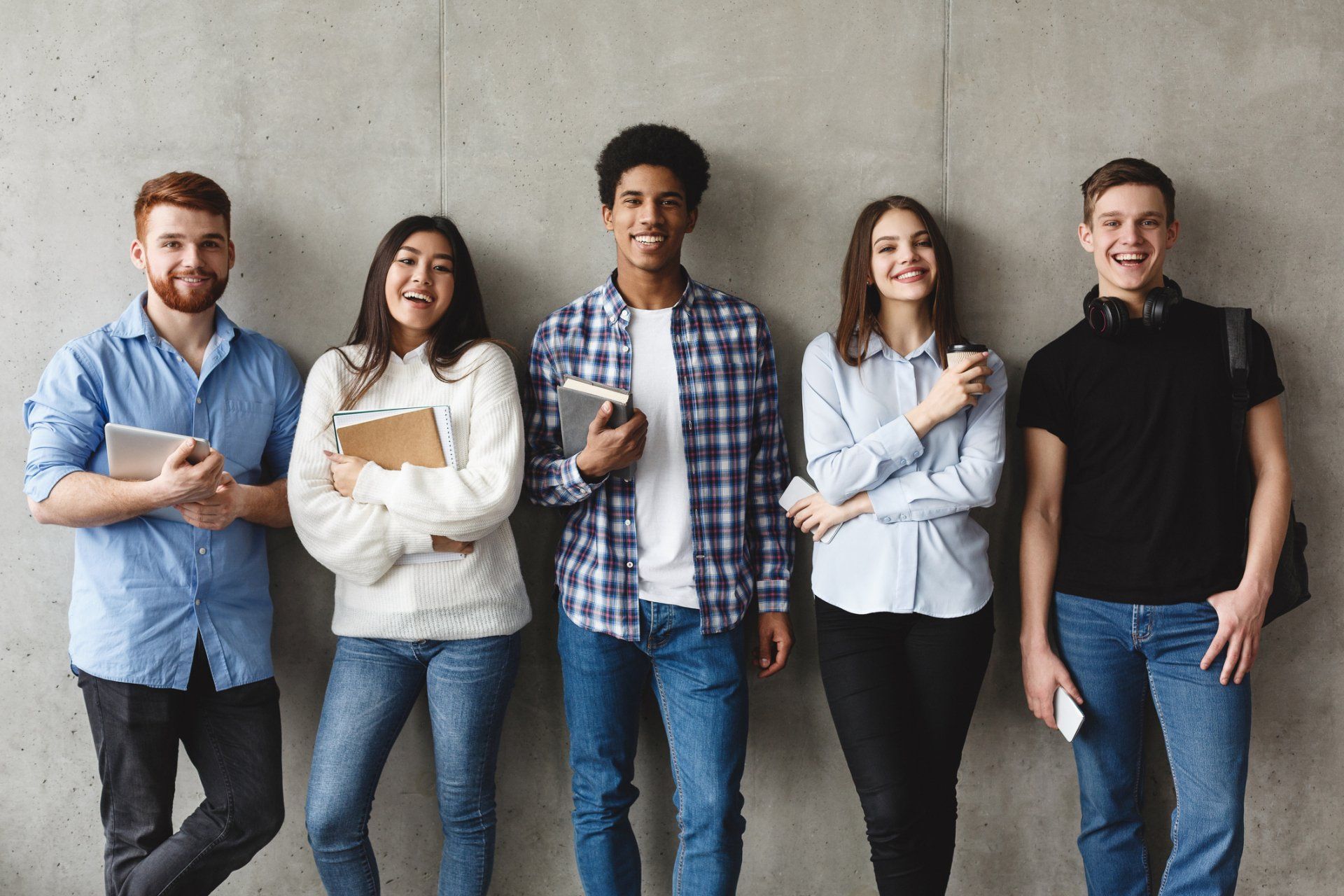 College students with books smiling to camera over grey wall — Clarkston, WA — LifeTrack Services, Inc