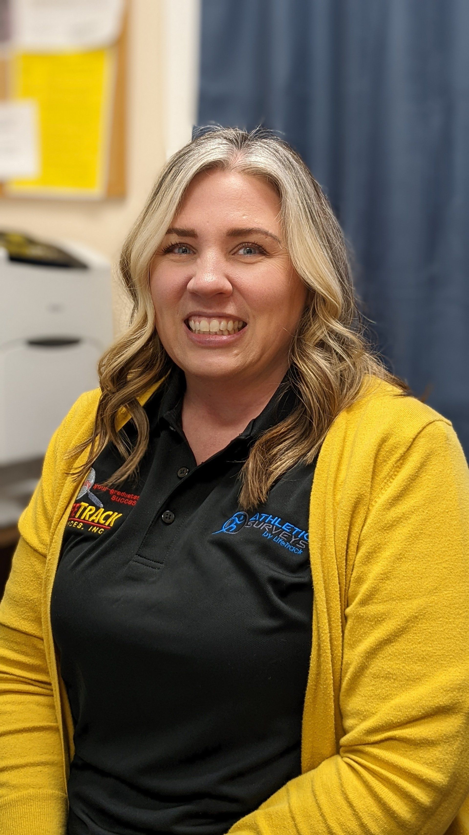 Woman wearing a yellow cardigan over a black polo shirt, smiling at the camera.
