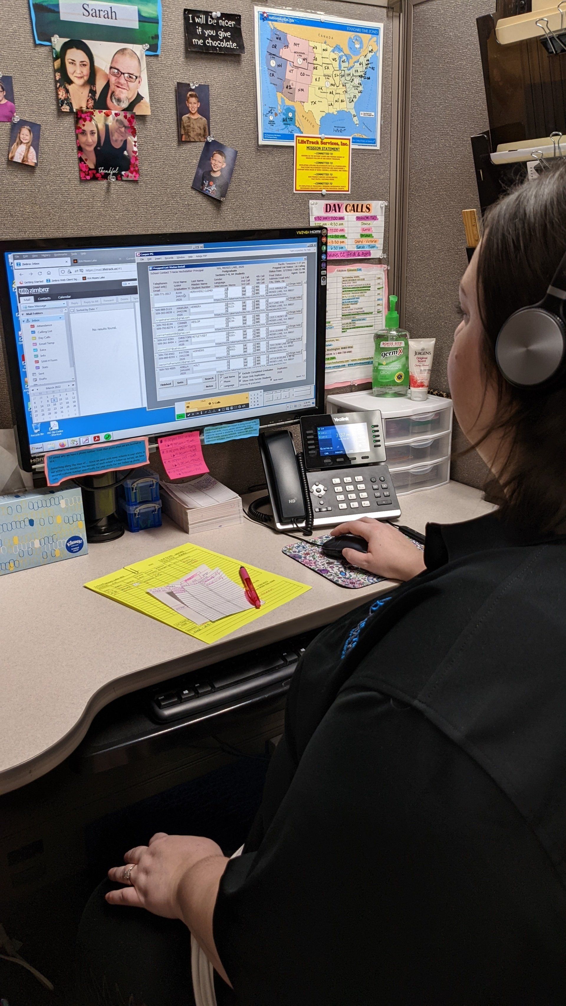 Person wearing a headset sits at a desk, looking at a computer screen. In an office setting, with a map and notes.
