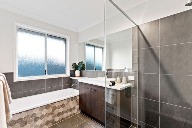 A bathroom with a tub , sink , mirror and shower. — Peter Betros Homes in Highfields, QLD
