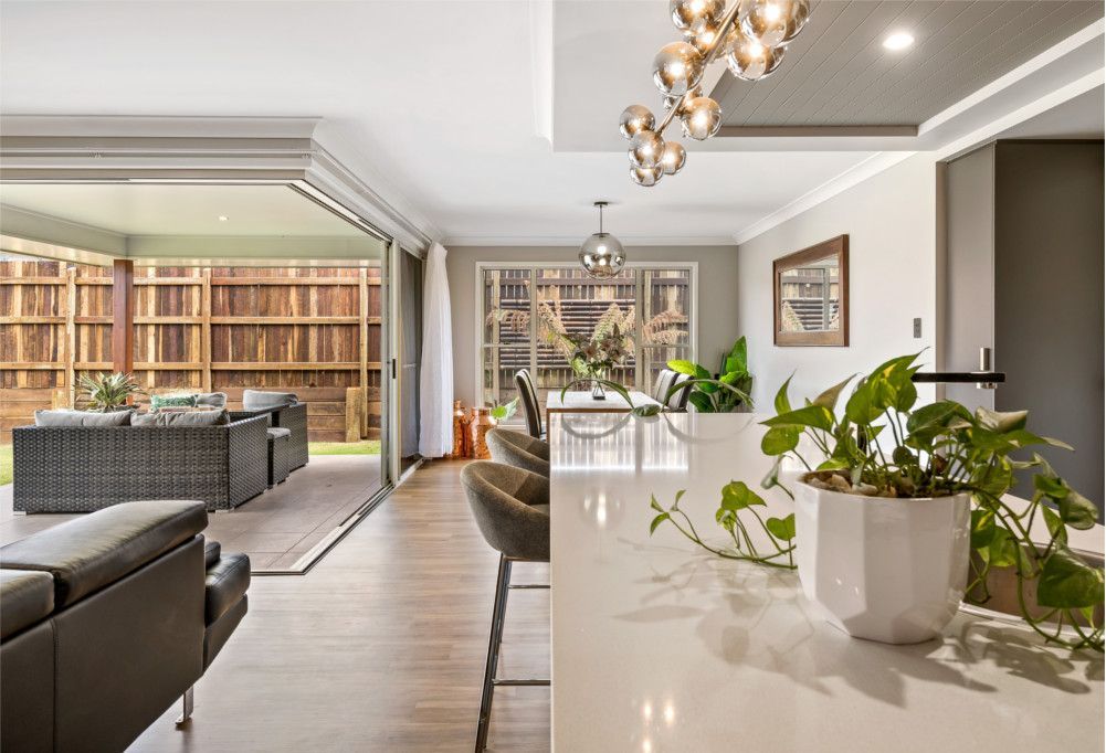 A living room with a couch , chairs , a table and a potted plant. — Peter Betros Homes in Highfields, QLD
