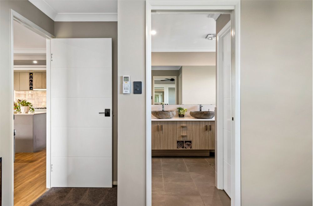 A hallway in a house leading to a bathroom with two sinks. — Peter Betros Homes in Highfields, QLD