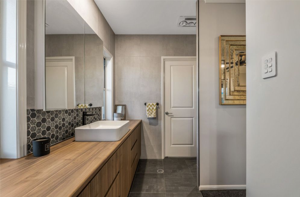 A bathroom with a sink , mirror and wooden cabinets. — Peter Betros Homes in Highfields, QLD