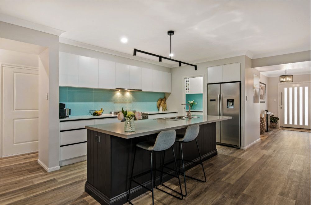 A kitchen with a large island and stools and a refrigerator. — Peter Betros Homes in Highfields, QLD