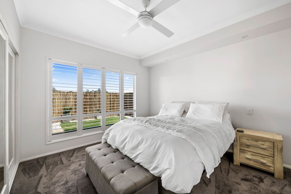 A bedroom with a large bed , a ceiling fan , and a window. — Peter Betros Homes in Highfields, QLD