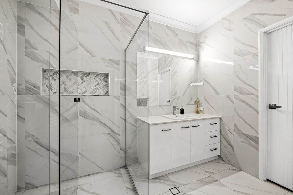 A bathroom with marble tiles , a sink , and a walk in shower. — Peter Betros Homes in Highfields, QLD