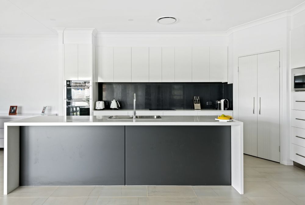 A kitchen with black and white cabinets and a large island — Peter Betros Homes in Highfields, QLD
