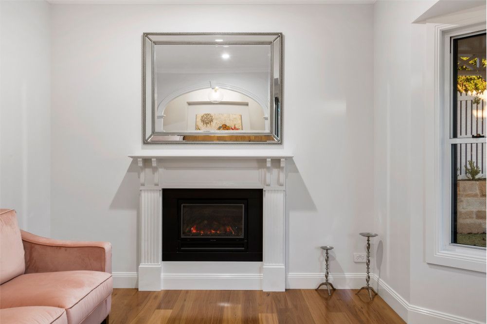 A living room with a fireplace , couch , mirror and window. — Peter Betros Homes in Highfields, QLD
