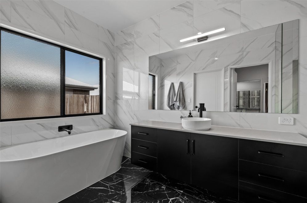 A Bathroom with A Bathtub, Sink, Mirror and Two Windows — Peter Betros Homes in Highfields, QLD