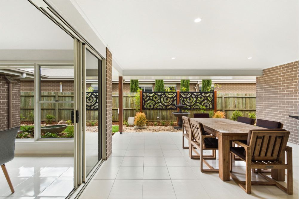 A dining room with a table and chairs and sliding glass doors leading to a patio. — Peter Betros Homes in Highfields, QLD