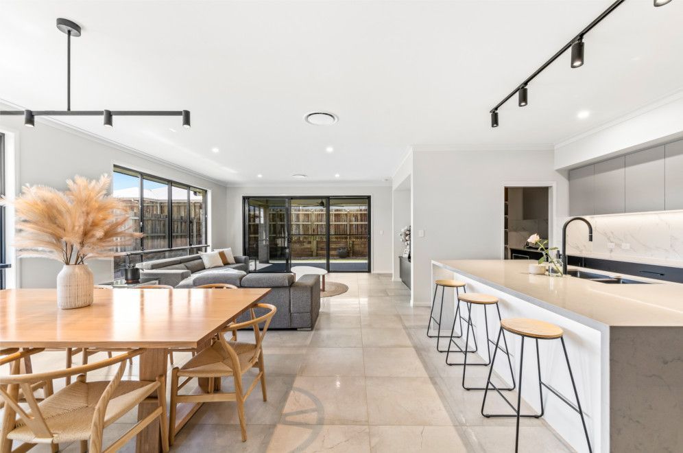 There is a dining table and chairs in the middle of the room. — Peter Betros Homes in Highfields, QLD