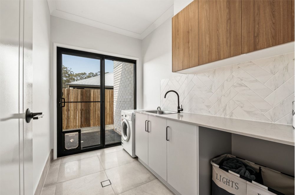 A laundry room with a washing machine , sink , and sliding glass doors. — Peter Betros Homes in Highfields, QLD