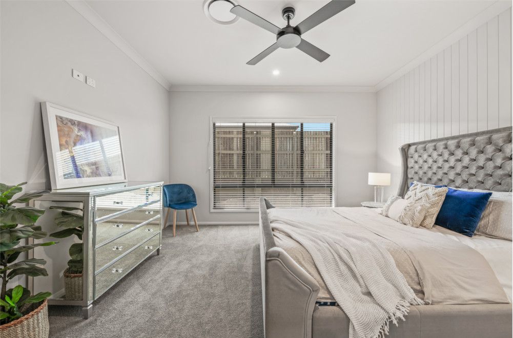 A bedroom with a bed , dresser , mirror and ceiling fan. — Peter Betros Homes in Highfields, QLD