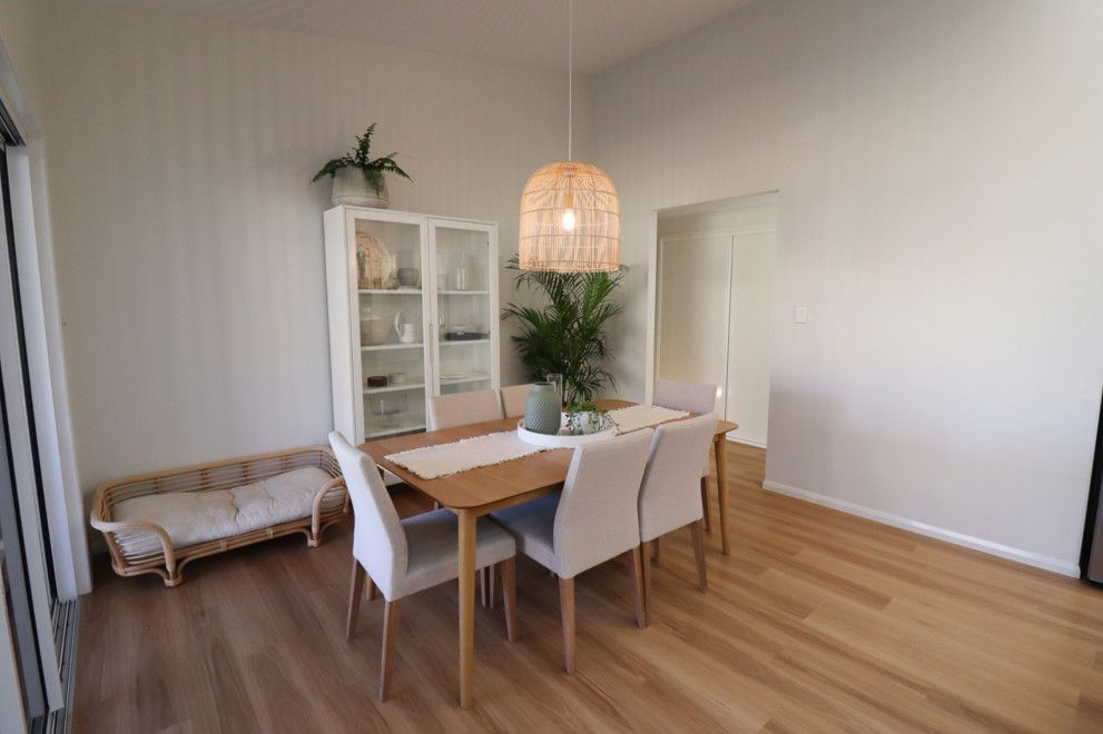 A dining room with a wooden table and white chairs. — Peter Betros Homes in Highfields, QLD