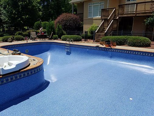 A large swimming pool with a jacuzzi next to it in front of a house.
