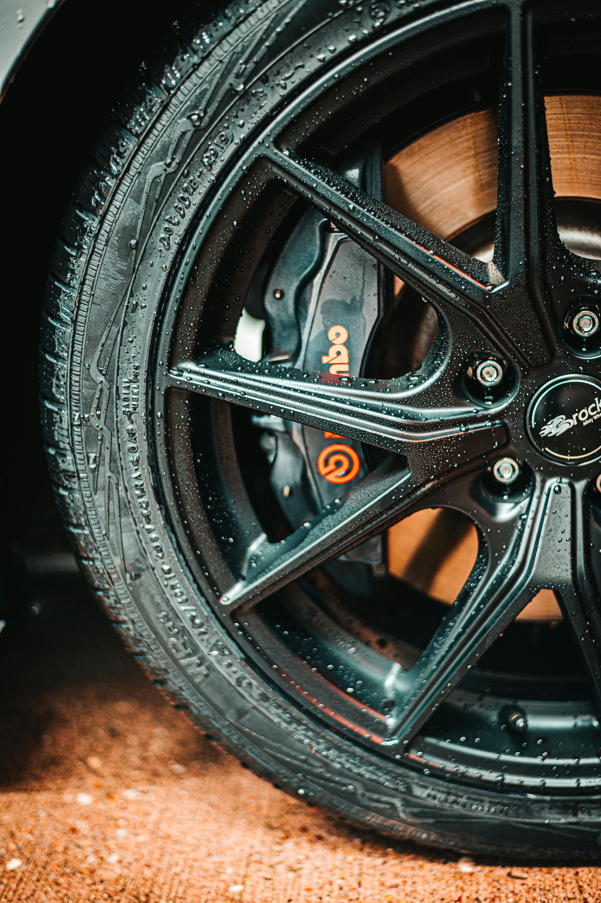 Close-up of a black car wheel with wet tire and glossy rim against a dark background