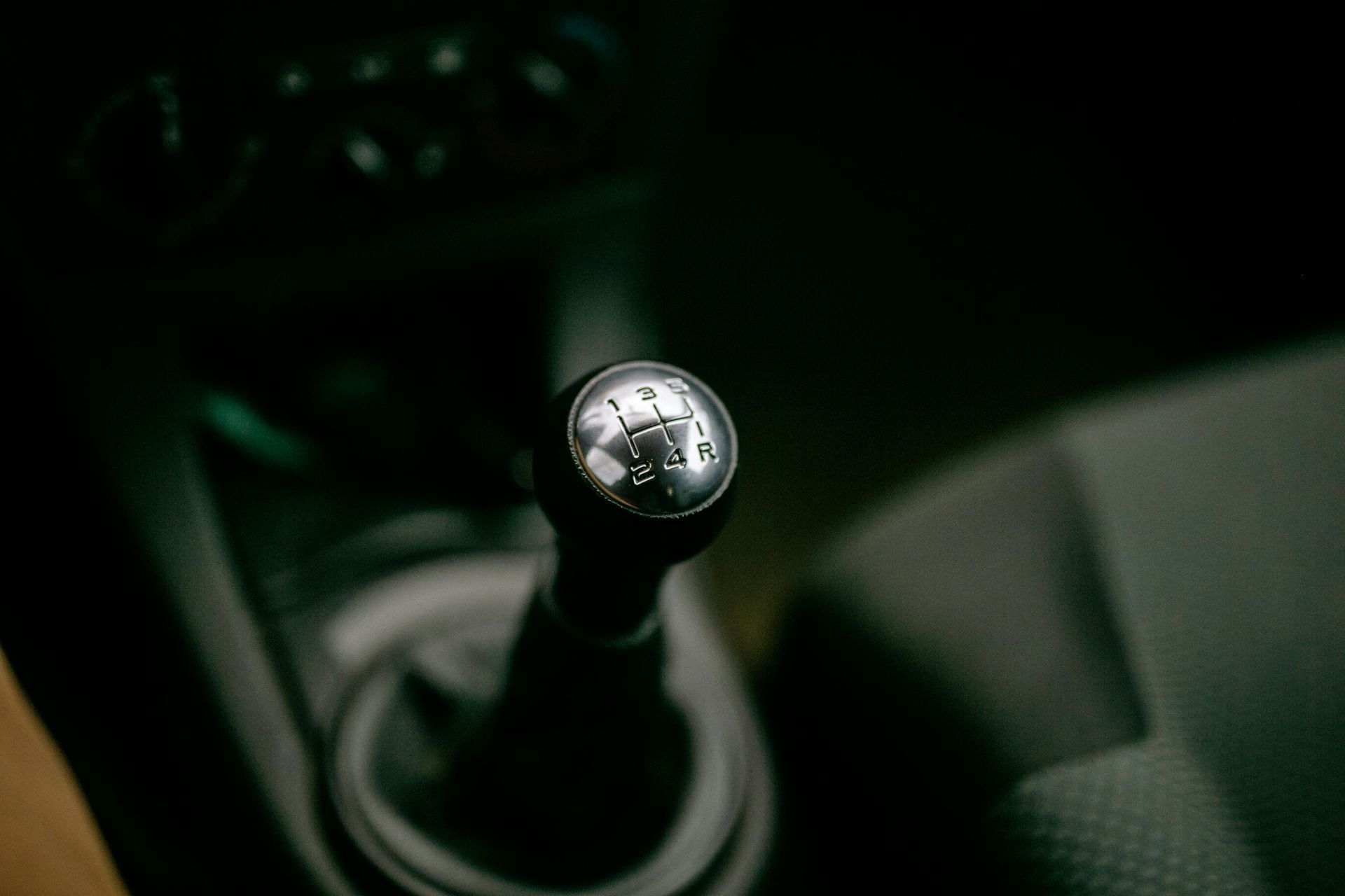 Close-up of a car’s manual gear shift knob in a dark interior.