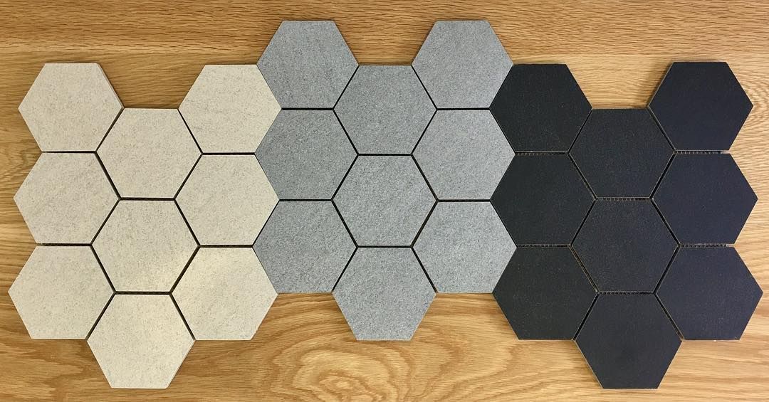 Three Different Colored Hexagon Tiles Are Sitting on a Wooden Table — Dean Gray Tiling in Robina, QLD
