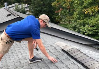 A man in a blue shirt and hat is kneeling on a roof.