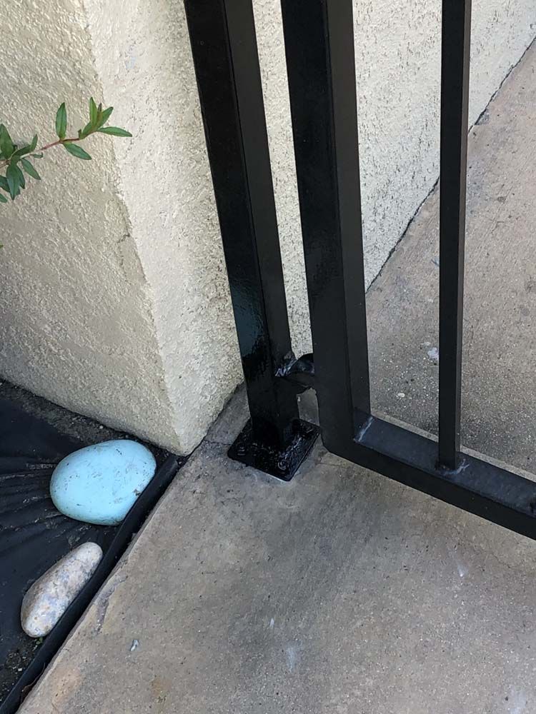 Black metal gate attached to a concrete wall and ground. A blue object rests near the wall.