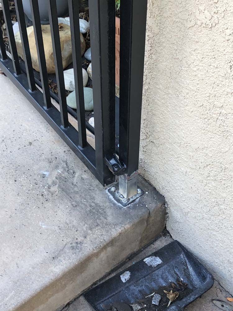 Black metal railing post secured to a concrete step.