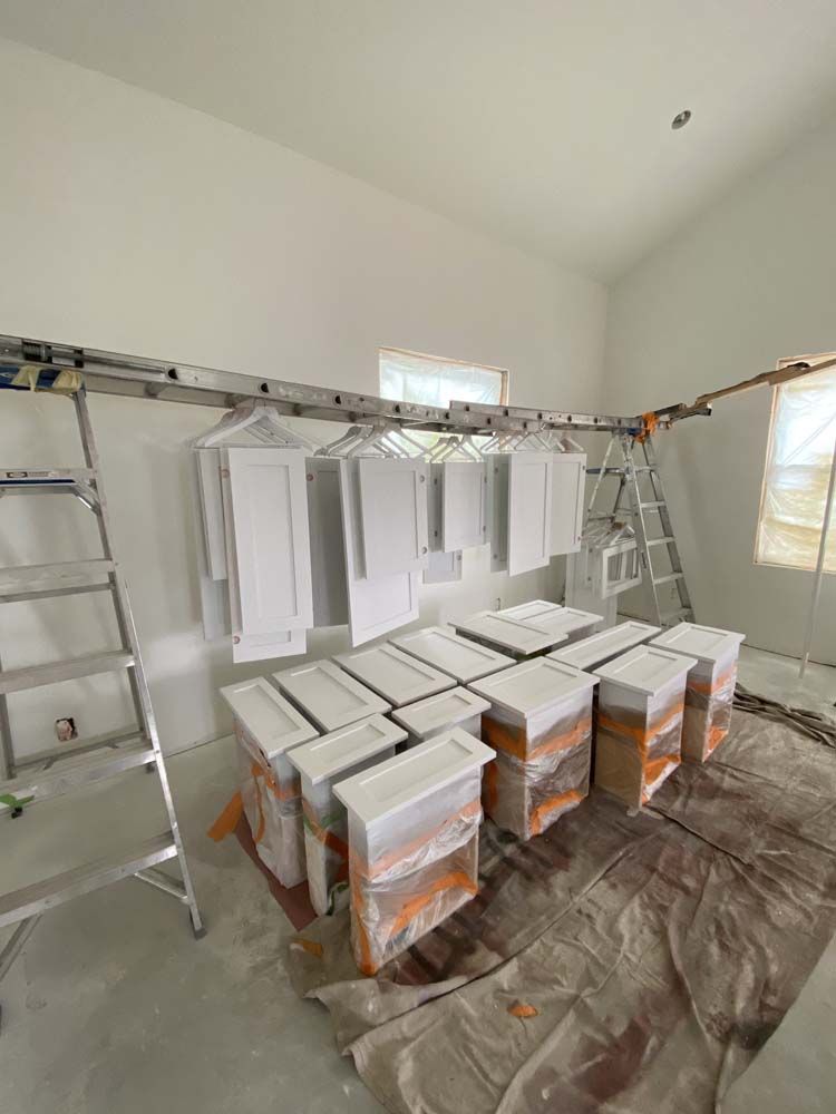 White painted cabinets hanging and stacked in a room during construction. Ladders and painting supplies present.