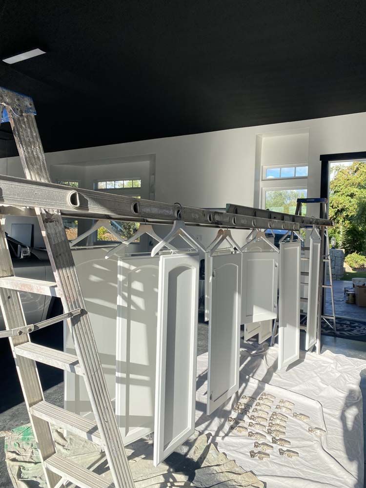 White cabinet doors hanging on a rack in a garage, waiting to dry after painting.