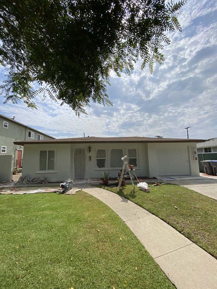 A light-colored house with a pathway and lawn under a cloudy sky. Construction materials are visible.