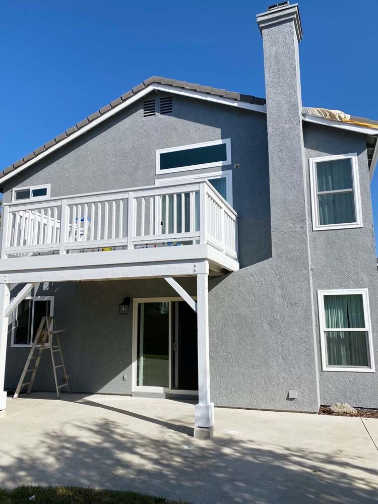 Gray stucco house with white deck and windows, chimney, and clear blue sky.