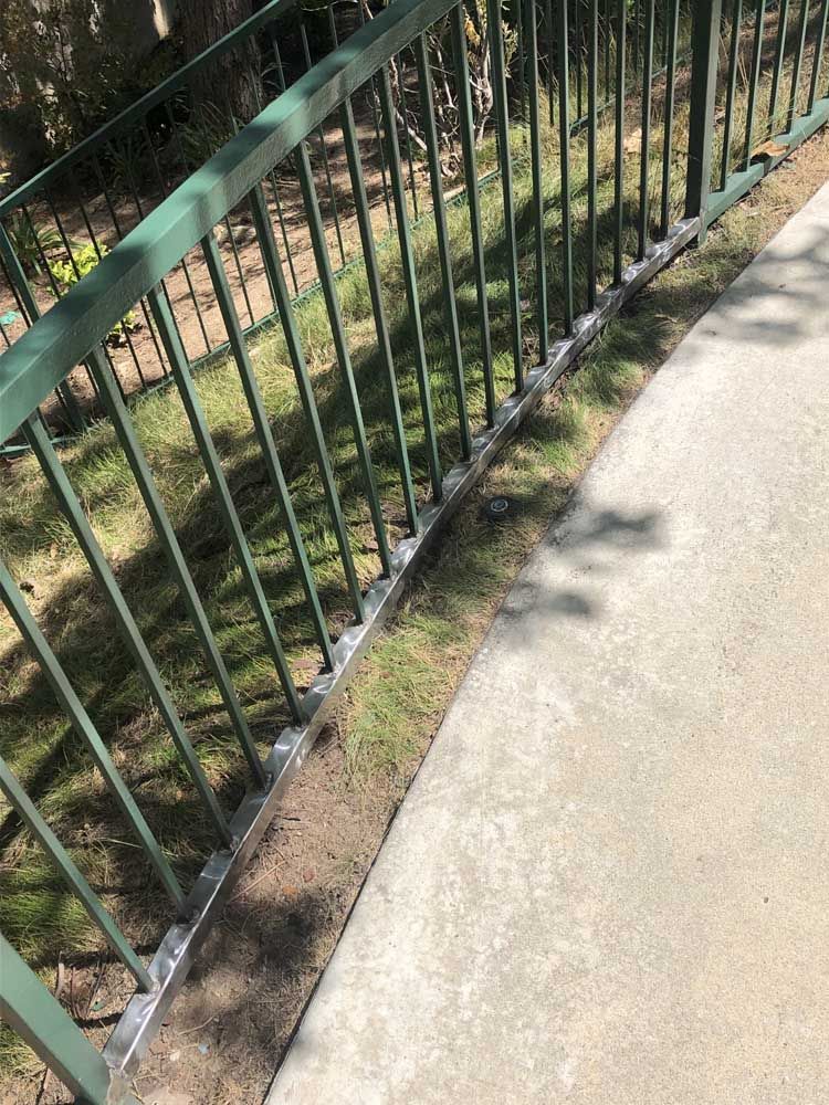 Green metal railing alongside a concrete walkway and grassy area.