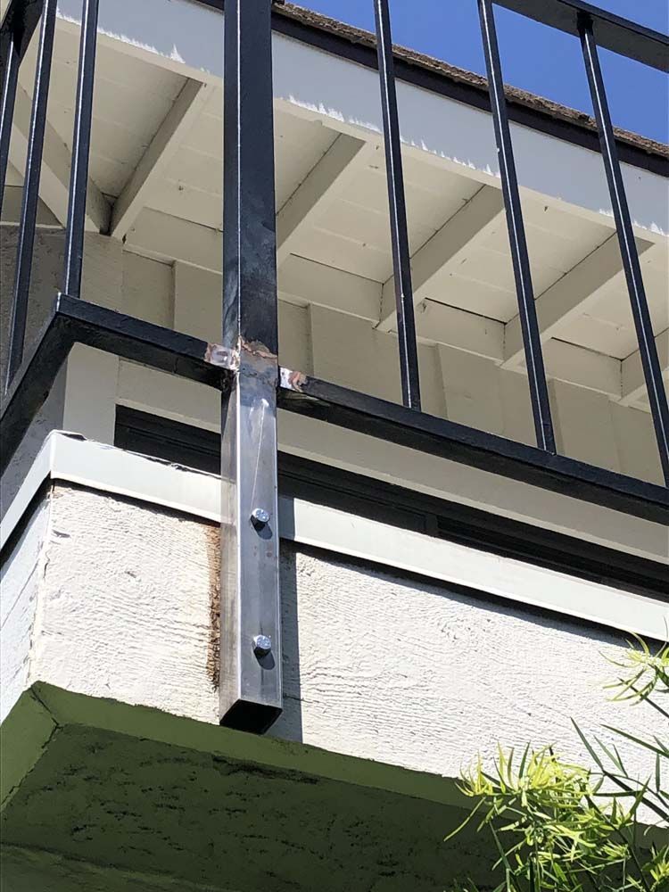 Black metal railing attached to a white stucco wall with bolts, blue sky in the background.