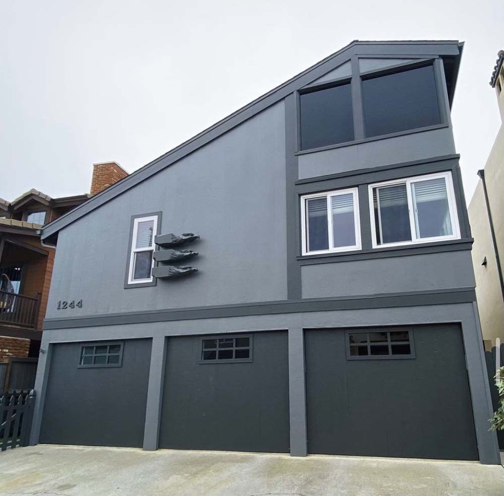 Gray beach house with three garage doors. Large windows and angled roof.