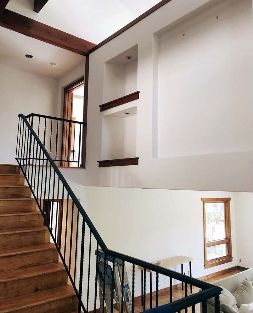 Staircase with wooden steps and black railing; white walls; built-in shelves; wooden beams and window frames.